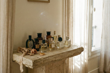 Curated collection of niche French perfume bottles displayed on an antique stone pedestal in an atelier.