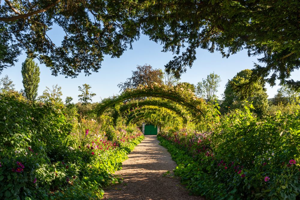 The central alley of the Clos Normand in Giverny featuring rose arches over a sunlit gravel path