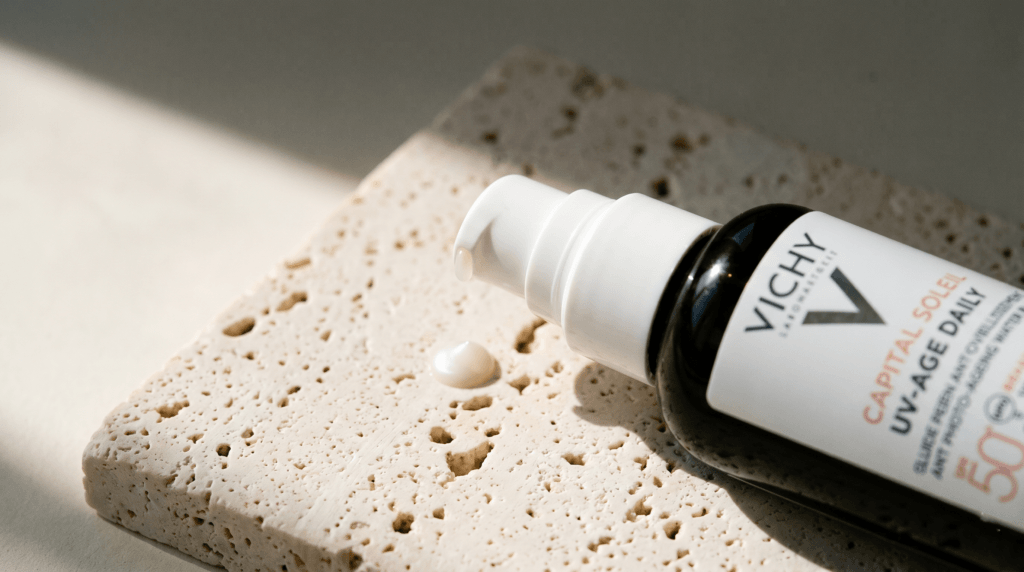 Vichy Capital Soleil UV-Age Daily SPF 50+ sunscreen bottle with a drop of product on a stone surface