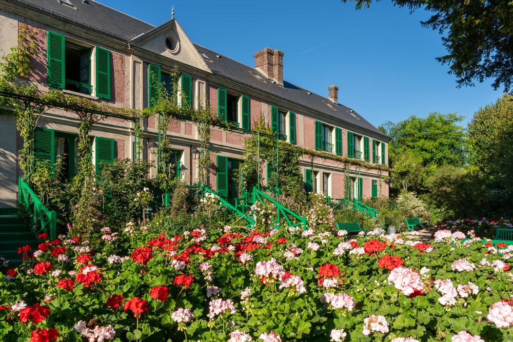 Claude Monet's pink house with green shutters in Giverny fronted by a field of blooming red and pink geraniums
