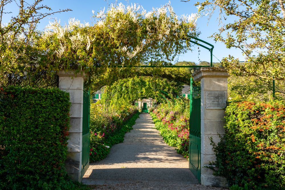 Open green gates of the Clos Normand in Giverny with a plaque commemorating Claude Monet's residence from 1883 to 1926