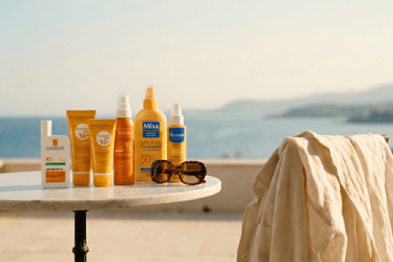 Selection of French pharmacy sunscreens including La Roche-Posay, Bioderma, and Avène on a table overlooking the Mediterranean sea