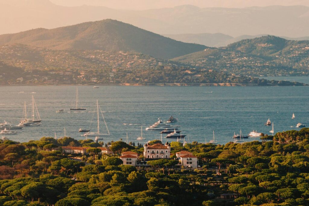 Drone shot of Château de la Messardière ochre turrets and pine forests overlooking yachts in the Saint-Tropez bay at sunset