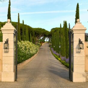 Entrance pillars of Airelles Château de la Messardière leading to a scenic cypress-lined driveway in Saint-Tropez
