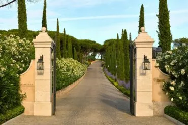 Entrance pillars of Airelles Château de la Messardière leading to a scenic cypress-lined driveway in Saint-Tropez