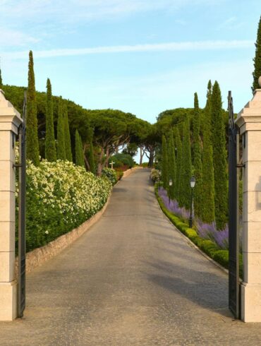 Entrance pillars of Airelles Château de la Messardière leading to a scenic cypress-lined driveway in Saint-Tropez