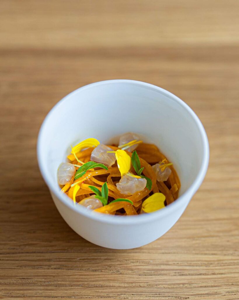 Gourmet appetizer with julienned vegetables and edible yellow petals served in a white ceramic bowl