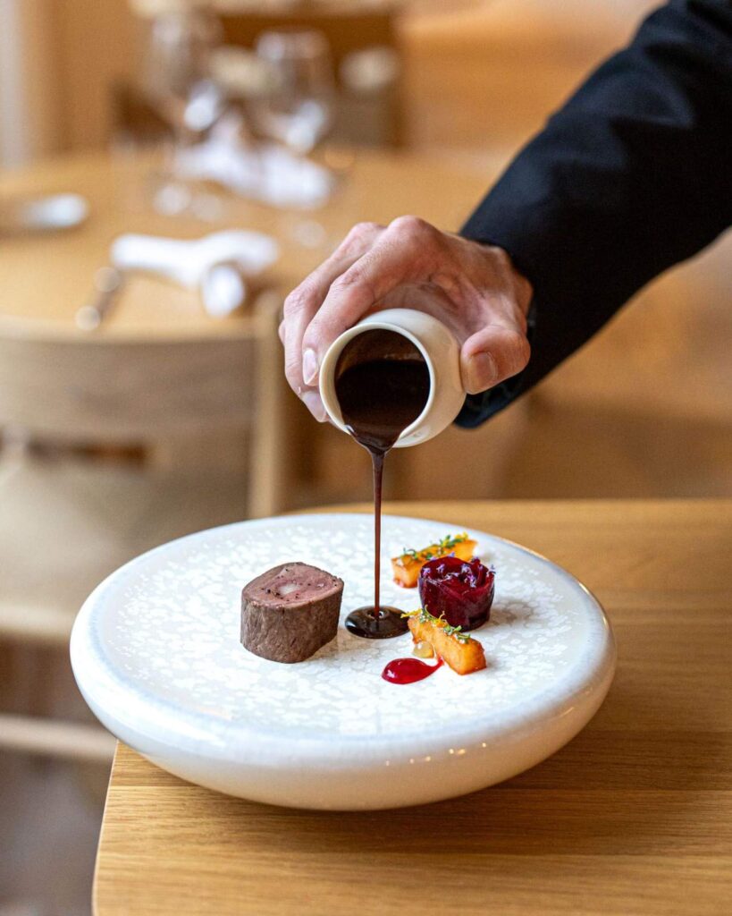 Chef pouring a dark reduction sauce over a gourmet meat dish at the La Feuillée gastronomic restaurant
