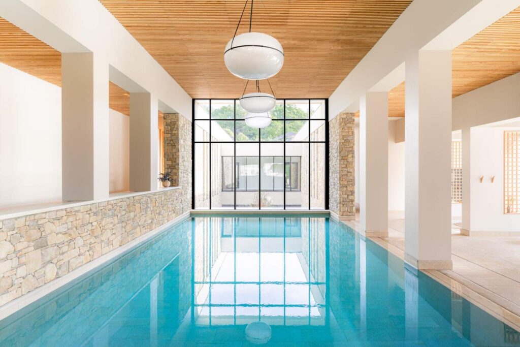 Modern indoor lap pool with stone walls and minimalist globe lighting at the Couvent des Minimes wellness center