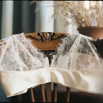 An alabaster silk and Calais lace bralette draped elegantly over a walnut chair in a sun-drenched Parisian apartment