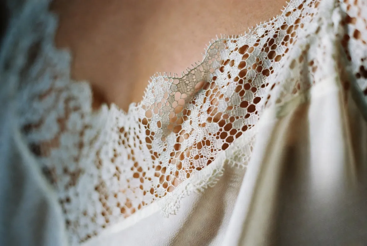 A detailed macro photograph highlighting the intricate weaving of authentic Calais-Caudry lace on an alabaster silk camisole. french lingerie