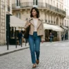 A French woman walks in Saint-Germain-des-Prés wearing a sand-colored cropped trench coat over raw denim and Mary Janes.