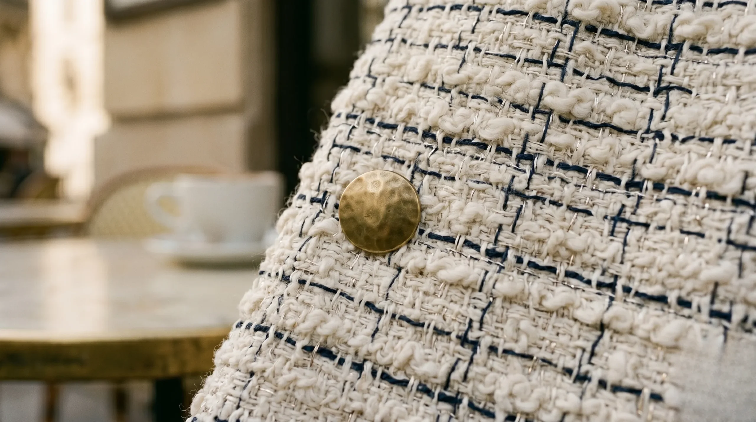 A macro close-up of a cream and navy woven bouclé fabric showing fine metallic threads and a brass button.