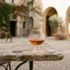 A classic crystal glass of amber cognac on an antique stone table in a French estate garden.