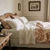 An elegant French manor bedroom with raw linen and sienna-toned Toile de Jouy bedding on a sunny morning