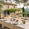 An elegant sun-drenched stone terrace in Provence featuring a dining table set with linen, ceramic plates, and rosé wine under soft olive tree shadows.
