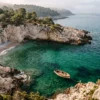 A quiet, pristine rocky cove along the Mediterranean coast in France with deep emerald water and a vintage wooden rowboat.