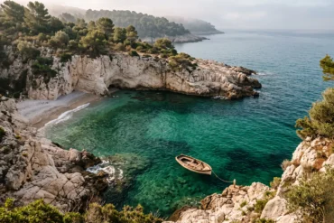 A quiet, pristine rocky cove along the Mediterranean coast in France with deep emerald water and a vintage wooden rowboat.
