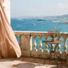 An elegant luxury hotel balcony with sienna linen curtains overlooking the blue waters of the Baie des Anges in Nice, France
