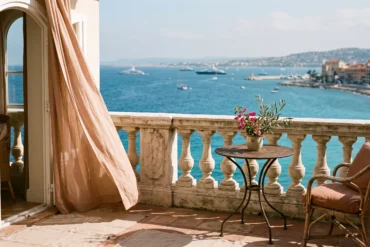An elegant luxury hotel balcony with sienna linen curtains overlooking the blue waters of the Baie des Anges in Nice, France